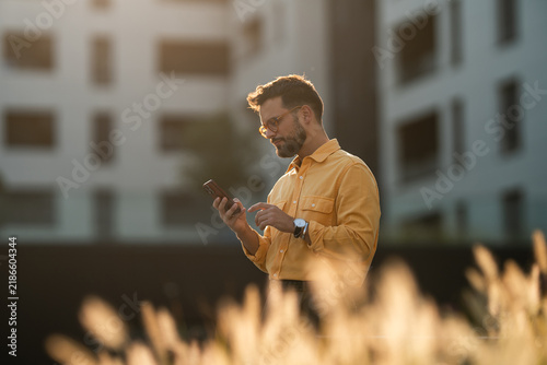 Bild auf Leinwand Young man using smartphone outdoor during golden hour