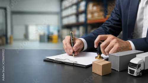 Businessman sealing contract with stamp beside shipping parcel and delivery truck in warehouse setting