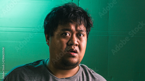 Canvas Print A young indonesian male stares directly at the camera with a stunned, confused, and slightly frightened expression in front of a green textured surface