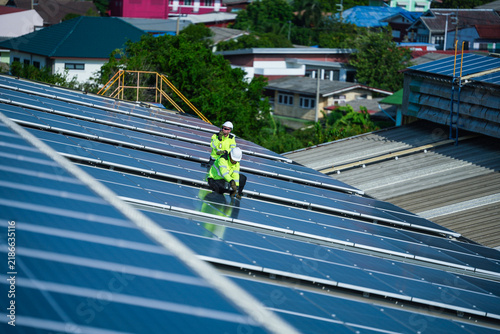 Fotografía A solar installation engineer in a white helmet and high visibility vest precisely inspects the huge array, a small figure among the panels high on an industrial warehouse roof in a Thai