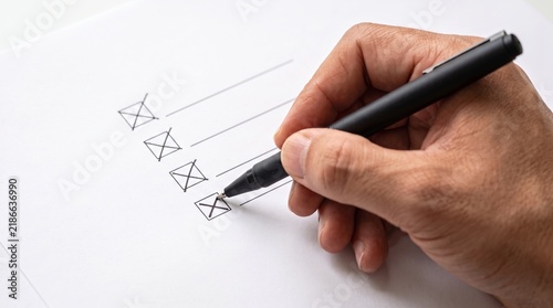 Hand marking a checklist with a pen on white paper