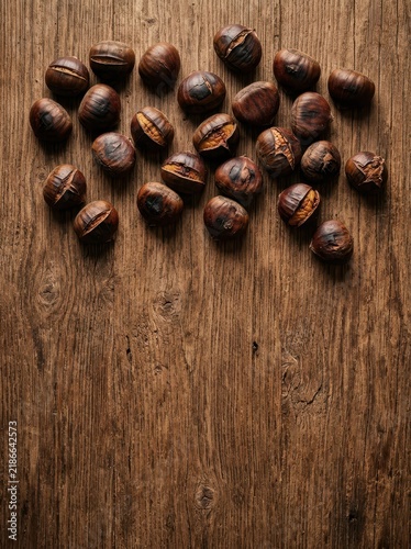 Overhead view of a cluster of roasted chestnuts scattered across a rustic wooden table, showcasing their rich brown color and