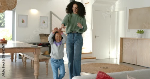 African American mother lifting child's hands, twirling, jumping at home, smartwatch cueing play