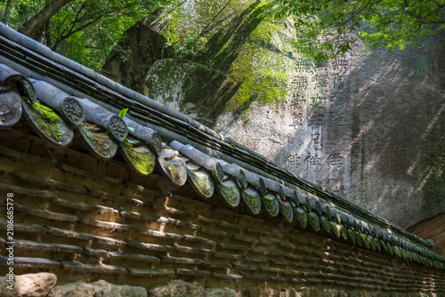 Foto A traditional Korean tiled earthen fence with mossy lotus eaves rises before a cliff carved with Buddhist prayers