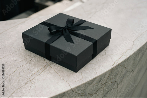 Matte black gift box with black satin ribbon on gray marble, minimalist luxury still life