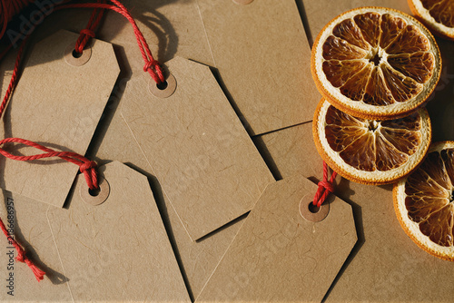 Blank kraft gift tags with red strings and dried orange slices, rustic flat lay