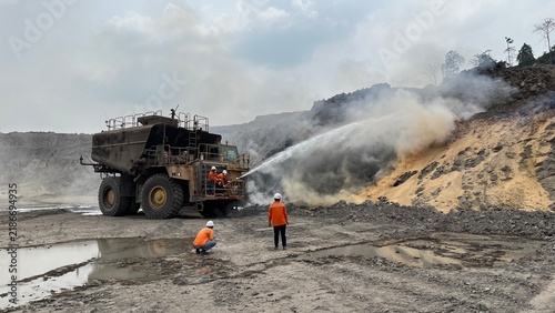 Water truck spraying high pressure water canon to extinguish fire and suppress dust at open pit coal mining site with miners observing