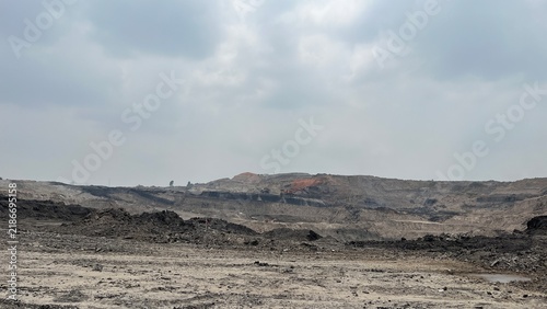 view of open pit coal mining area under cloudy overcast sky.