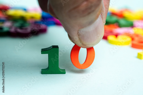 Принти на полотні Hand placing orange number ten among colorful numbers