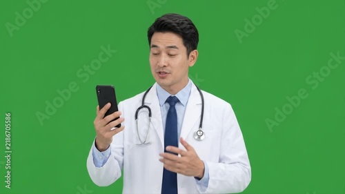 Male doctor providing a telemedicine consultation using a smartphone against a clean green screen background for digital healthcare and remote medical concepts.
