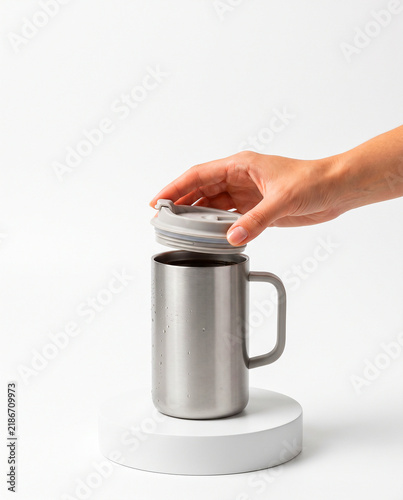 Hand Opening Lid of Stainless Steel Travel Mug on White Podium
