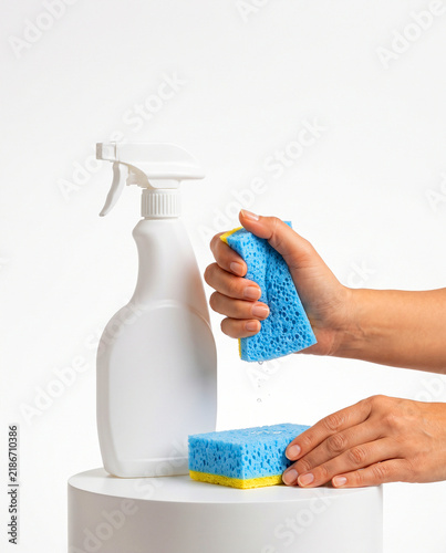 Hand Squeezing Blue Cleaning Sponge near White Spray Bottle on Podium
