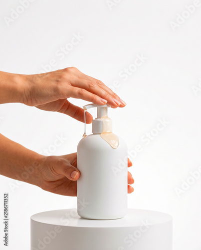 Hand Pressing White Soap Dispenser Bottle on White Round Podium
