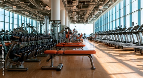 Empty modern gym interior with rows of treadmills and weight benches
