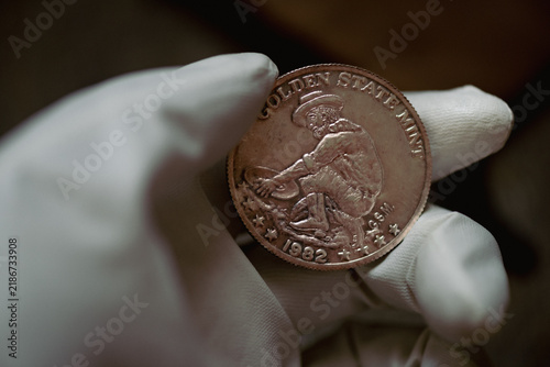Quadro su tela Close-up photo of a vintage American Golden State Mint one ounce silver round held with white gloves, featuring a classic gold prospector design, 1982 date and raised inscription