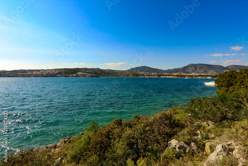 Foto Turquoise sea water gently lapping a green, rocky coastline with a distant town