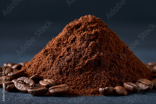 A small mound of finely ground coffee powder surrounded by dark roasted coffee beans