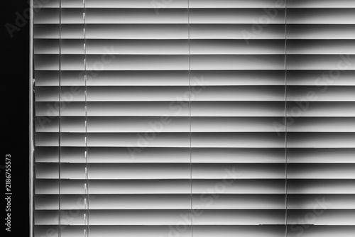 Closed horizontal window blinds in black and white create repeating lines, soft gradients and shadow patterns for a minimalist interior, privacy concept, architectural detail, or abstract backgrounds