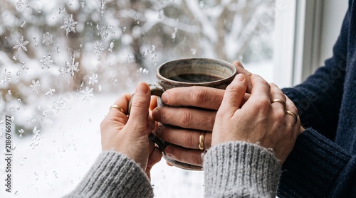 Cozy Winter Moment of a Person Holding a Warm Cup of Coffee by a Snowy Window