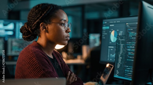 Focused Female Software Engineer Working on Computer in Dark Office.