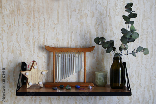 Foto Shelf in living room with small lamp, wind musical chimes, vase with eucalyptus, stone glass and six small colorful stones