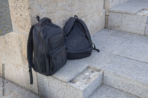 Two black backpacks resting on worn stone steps beside a wall