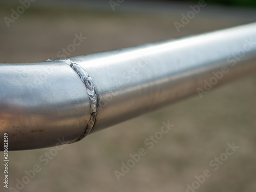 Close-up of a welded joint on a stainless steel tube, showing the visible weld bead and curved metal connection used in railing, fabrication and structural metalwork.