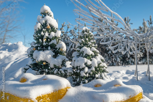 Outdoor Christmas display with snow-covered decorated trees, golden baubles and reindeer figures beneath a clear blue winter sky.2027