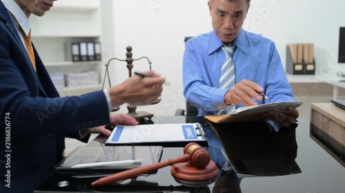 Professional lawyer advising a client, reviewing a contract and financial documents in a modern office with scales of justice