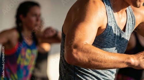 Close-up of sweaty muscular man during a vigorous fitness class, with blurred participants in the background.