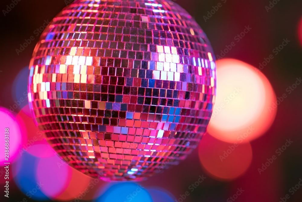 Obraz premium Close-up of a mirrored disco ball composed of hundreds of tiny reflective tiles catching magenta cyan and golden light against a dark background with large colorful bokeh circles creating a festive