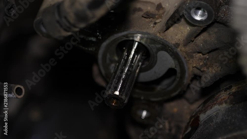 A close-up view shows an exposed splined shaft extending from a greasy and dirty automotive component during engine maintenance.