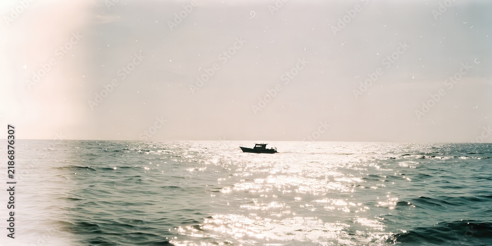 Obraz premium Small boat floating on shimmering ocean under sun