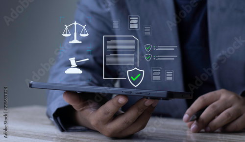 Legal compliance and regulatory verification concept with businessman holding tablet displaying glowing scales of justice, gavel, document shield, and checklist on dark background.