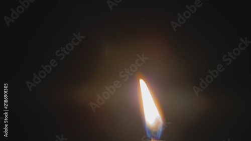 Candle flame glows softly against black background