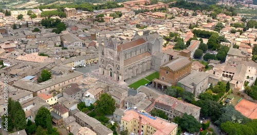 Aerial view of the facade of the Cathedral of Orvieto, in the province of Terni, in Umbria, Italy, with its walls striped in white and dark stone, surrounded by the rooftops of the historic center.