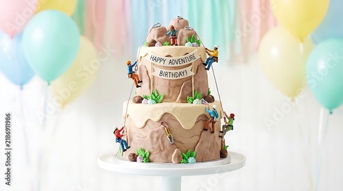 Two-tier mountain cake decorated with miniature climbers and colorful balloons