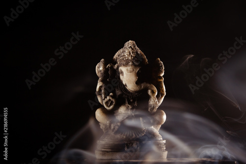 Lord Ganesha statue with incense smoke on black background for spiritual meditation concept.