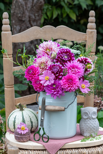 Blumenstrauß mit pink Dahlien, Herbstanemonen und Sommeraster im alten Emaille-Milchkrug auf einem Stuhl im Garten