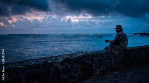 Contemplative old Azorean fisherman seated on a stone wall, gazing at the tranquil ocean at dusk; atmospheric lighting enhances the serene mood with dramatic clouds and distant boats.