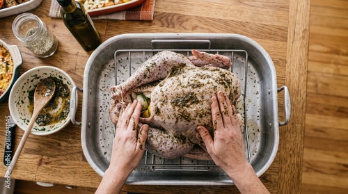 Hands preparing a golden brown roasted turkey in a disposable aluminum pan for a holiday feast