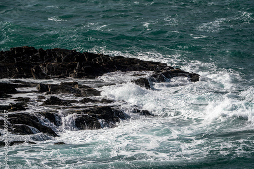 Crashing ocean waves breaking against dark jagged coastal rocks with foamy teal water and dramatic sea spray and surf