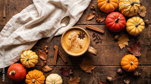 Warm autumn beverage with miniature pumpkins and colorful fall leaves on a rustic wooden surface