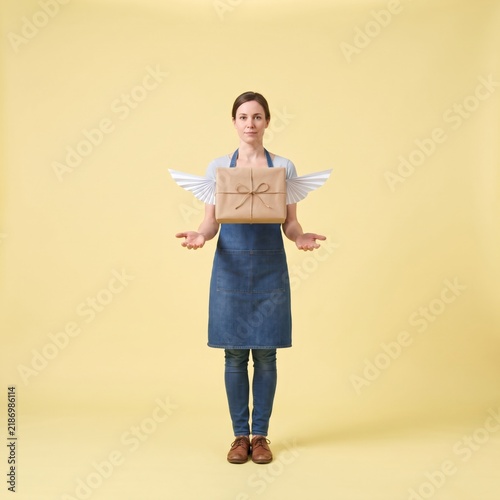Female business owner presenting winged flying package on yellow background for fast delivery concept