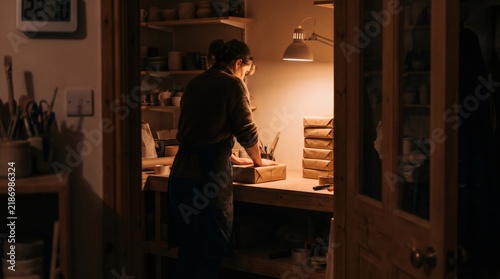 Focused artisan woman packing orders and sealing parcel in dark workshop late at night