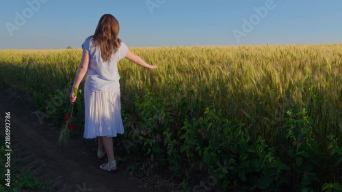 A beautiful young teenager girl in white dress walking along the edge of a ripe wheat field during golden hour, feeling free and peaceful in the countryside landscape