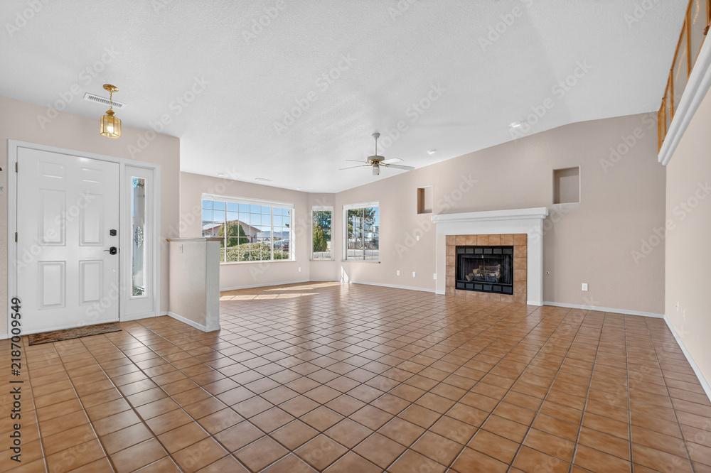 Naklejka premium Spacious living room with fireplace, large windows, beige walls, open plan, tiled floor sunlit view