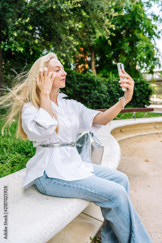 Blonde woman taking selfie with smartphone in park