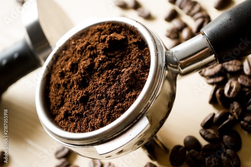 Quadro su tela Espresso machine filter holder filled with ground coffee powder with tamper and roasted beans on bright wooden table