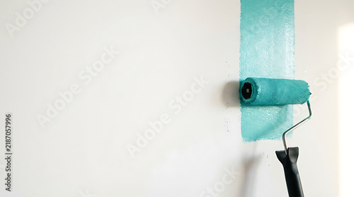 A close-up shot of a paint roller applying a vibrant turquoise color to a white interior wall, symbolizing home renovation, decorating, and a fresh start in living spaces